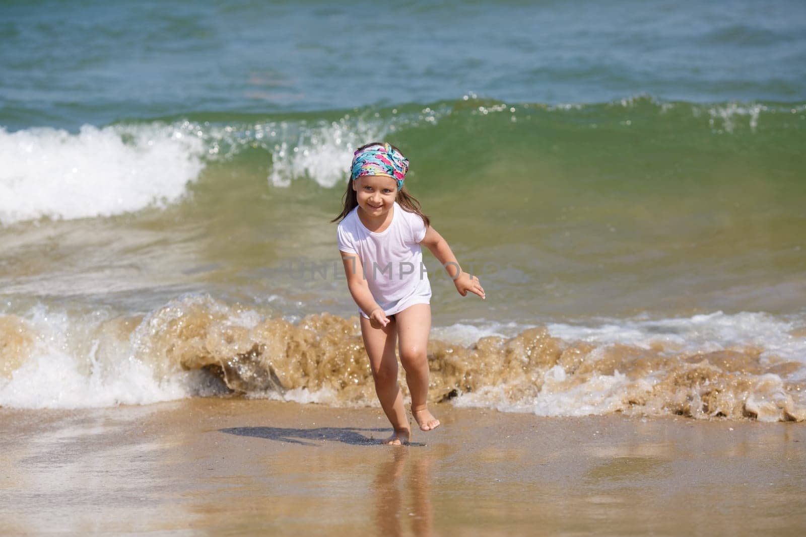 Child runs along the beach on a background of a sea wave. Shallow depth of field. Focus on model.