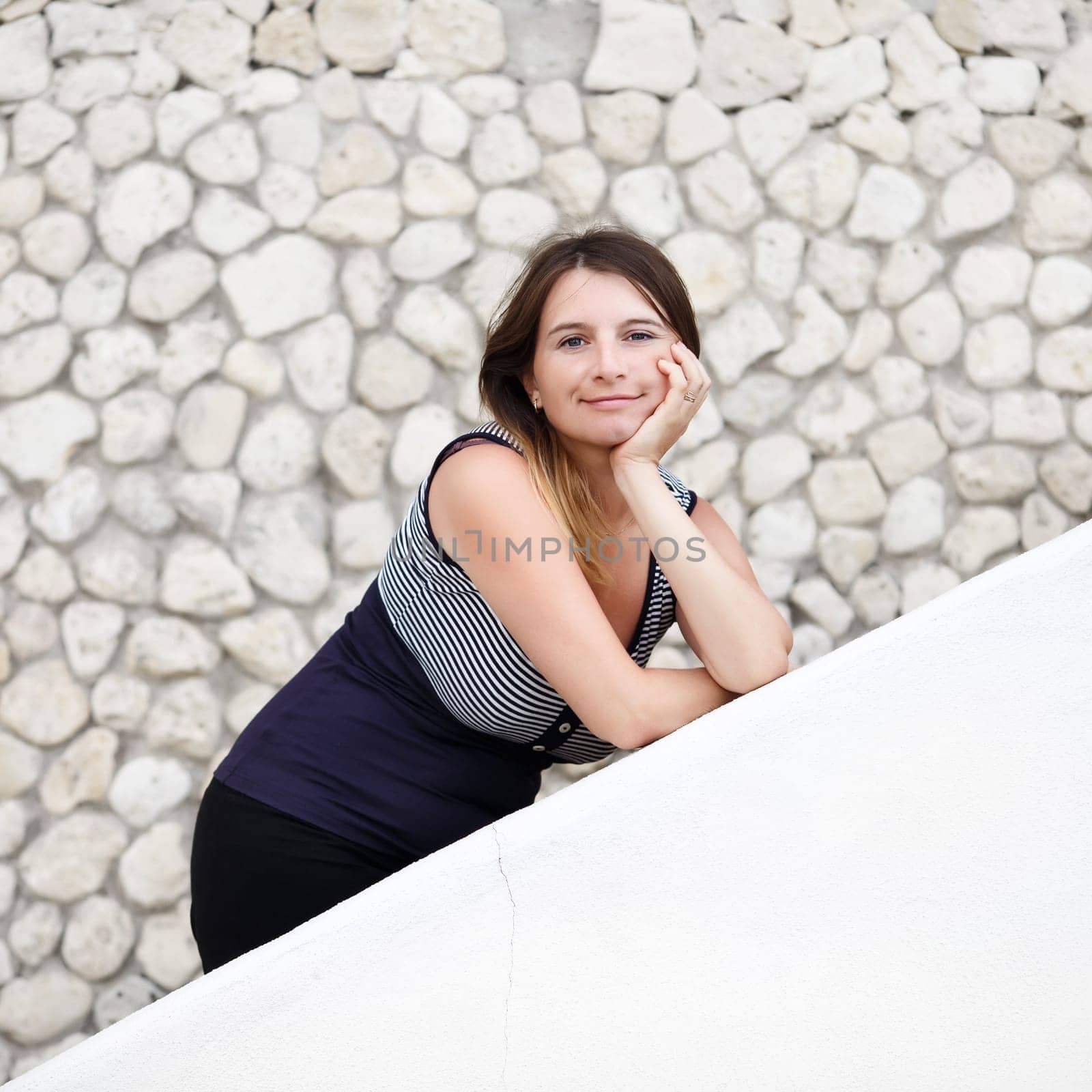Pretty young woman posing, leaning on the parapet on the background of old stone vintage wall. Selective focus on model. Photo in retro style.