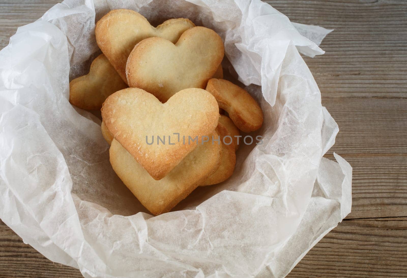 Cookies in the form of hearts in a paper wrapper on a wooden background. Top view.