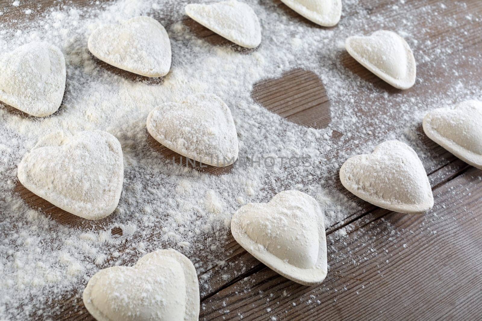Cooking ravioli. Raw dumplings in the form of hearts sprinkled flour on wooden background closeup. Shallow depth of field.
