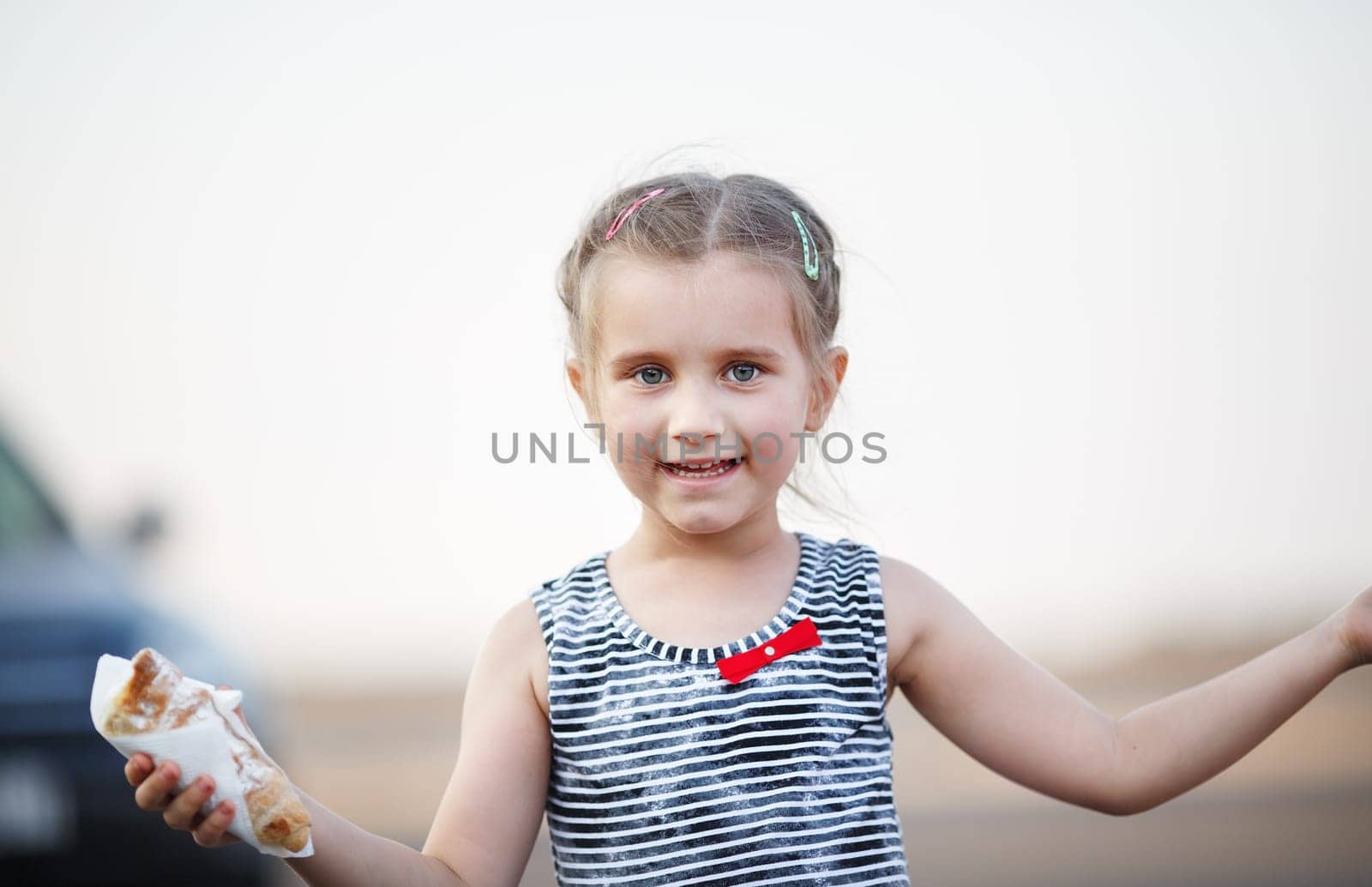 Close-up portrait of carefree happy smiling baby girl with a cake in hand.. Outdoors portrait of a child. Selective focus on model.