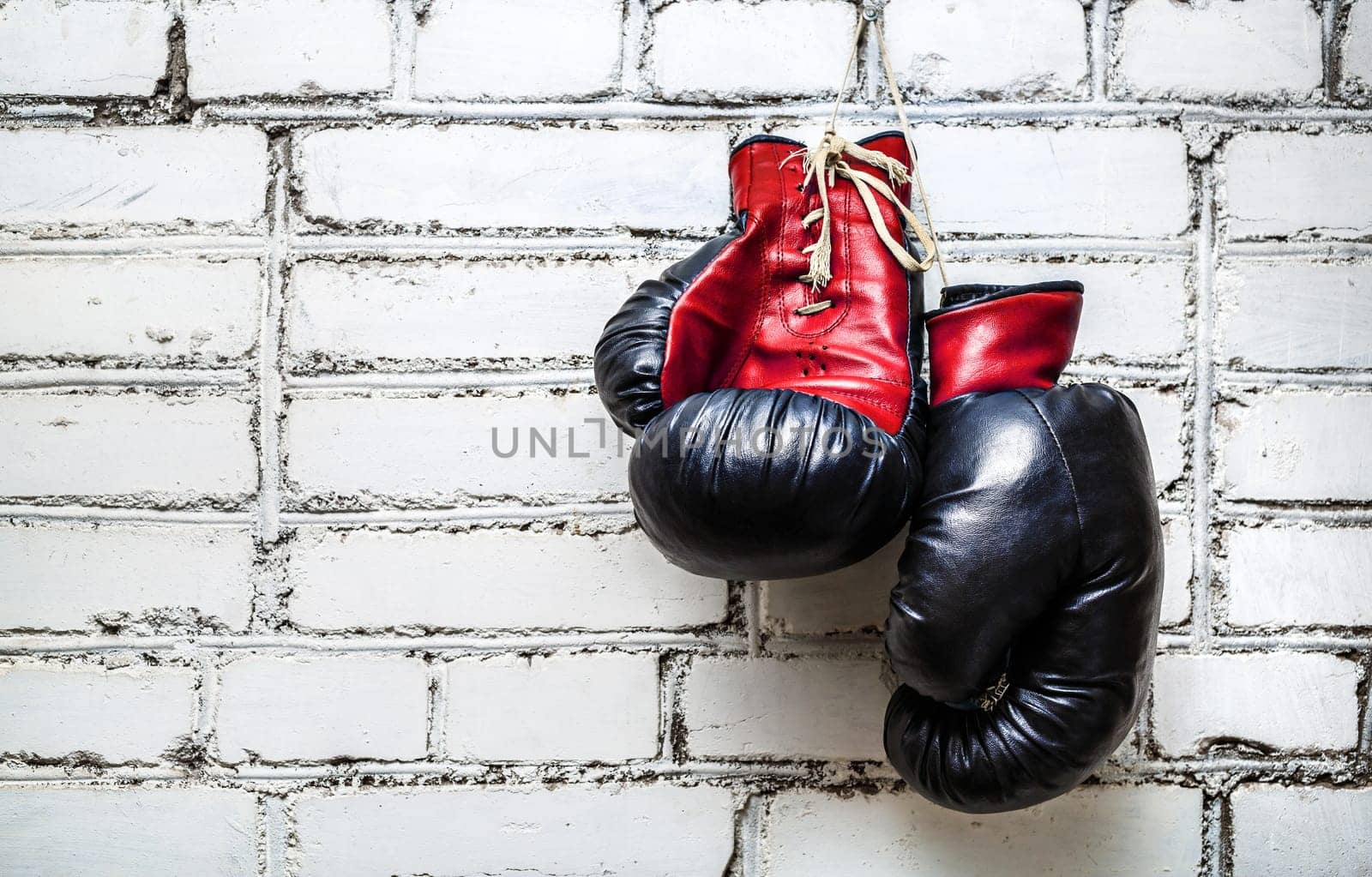 Pair of old red boxing gloves hanging on white brick wall.