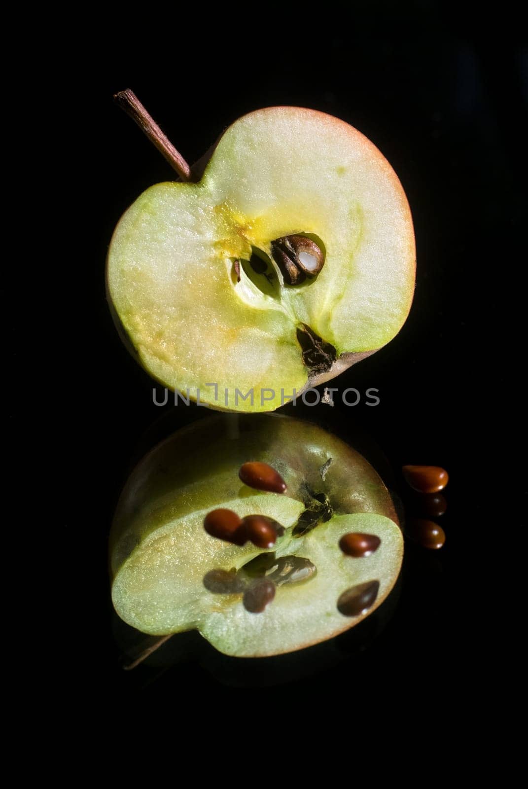 Apple cut in half with seeds on a black background with reflection. Vertical shot.