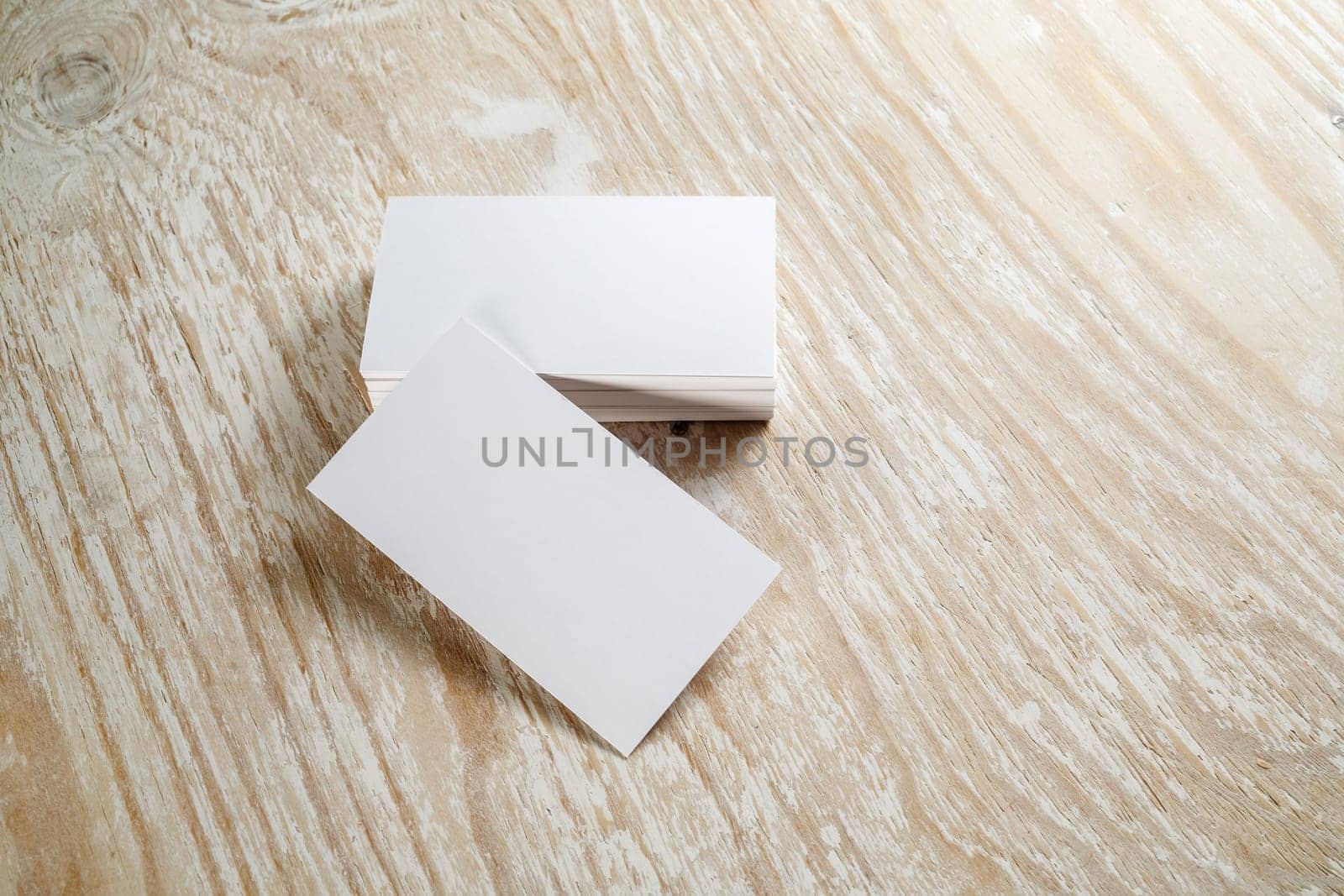 Photo of blank business cards with soft shadows on light wooden textured background. For design presentations and portfolios.
