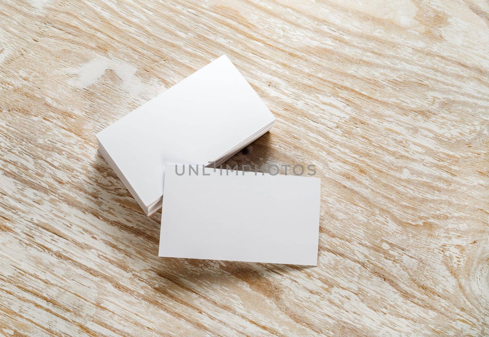 Blank business cards with soft shadows on light wooden background. Template for design presentations and portfolios. Studio shot.