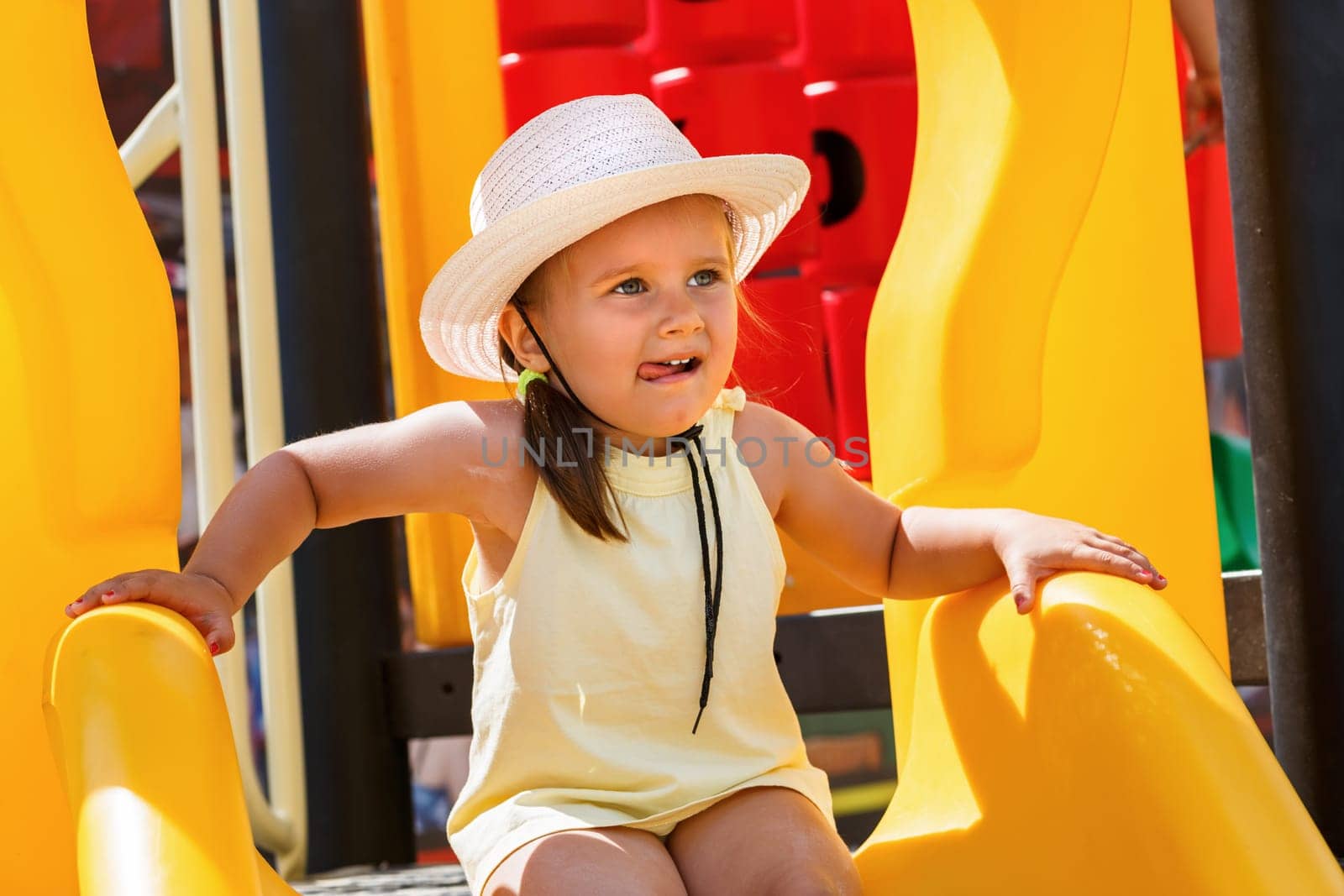 A child in a white hat and a yellow t-shirt on the playground on a sunny day. Shallow depth of field. Focus on the model's face.