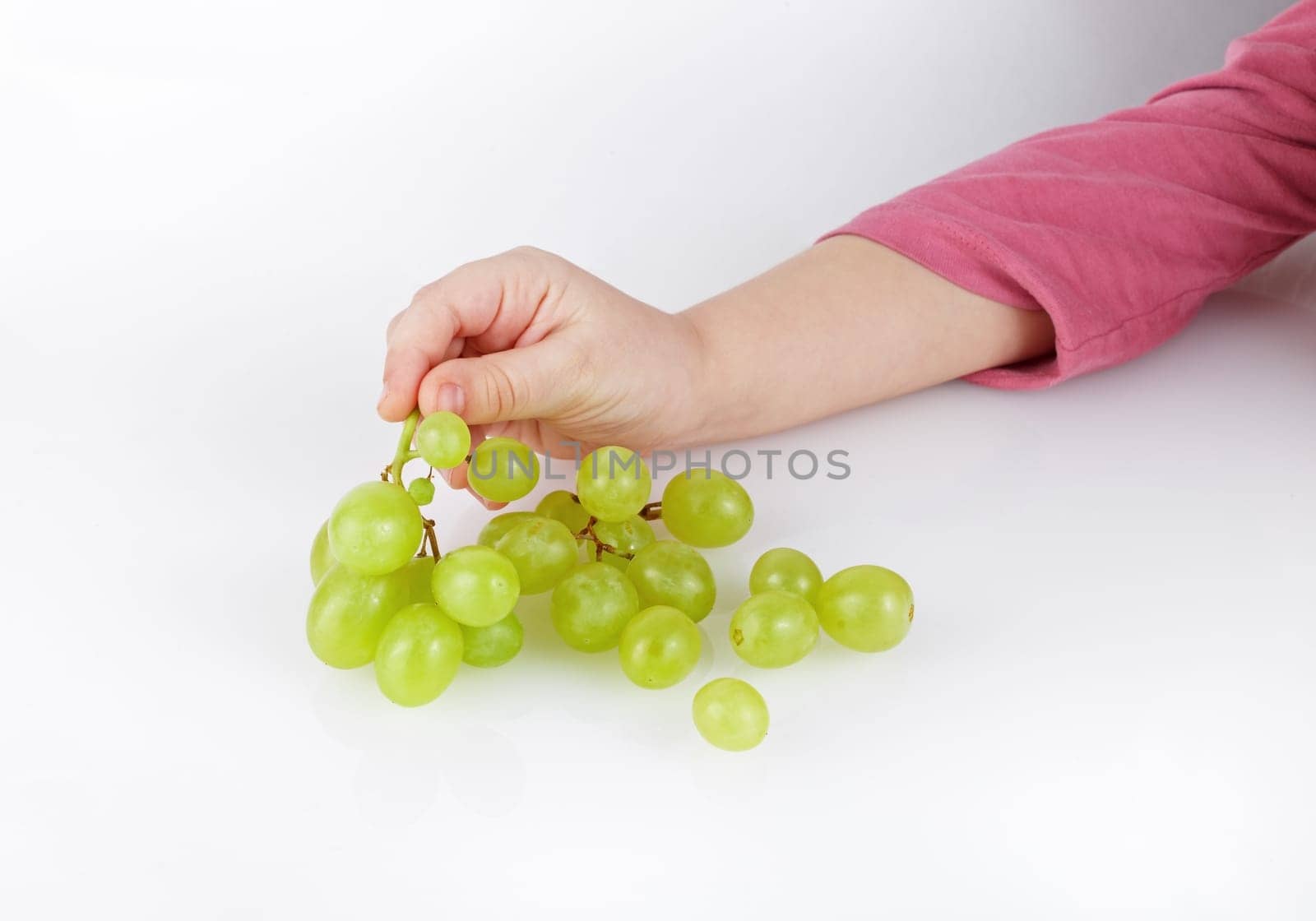 Children's hand takes a bunch of tasty green grapes.