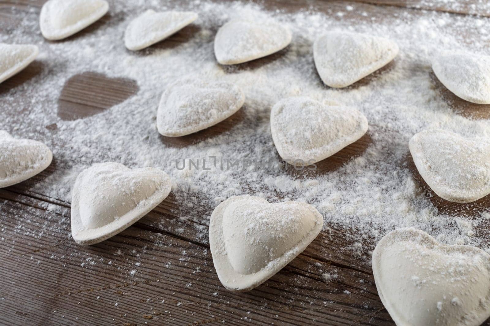 Raw ravioli in the shape of hearts, sprinkle with flour, on dark wooden background. Cooking dumplings. Shallow depth of field.