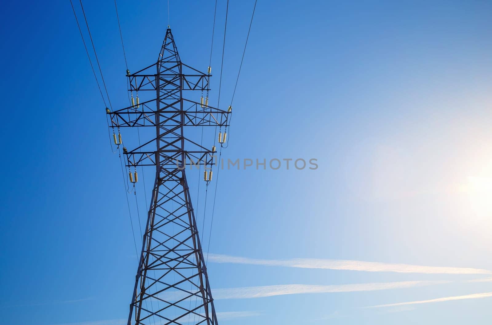 Electricity pylon silhouetted against blue sky background. High voltage tower.