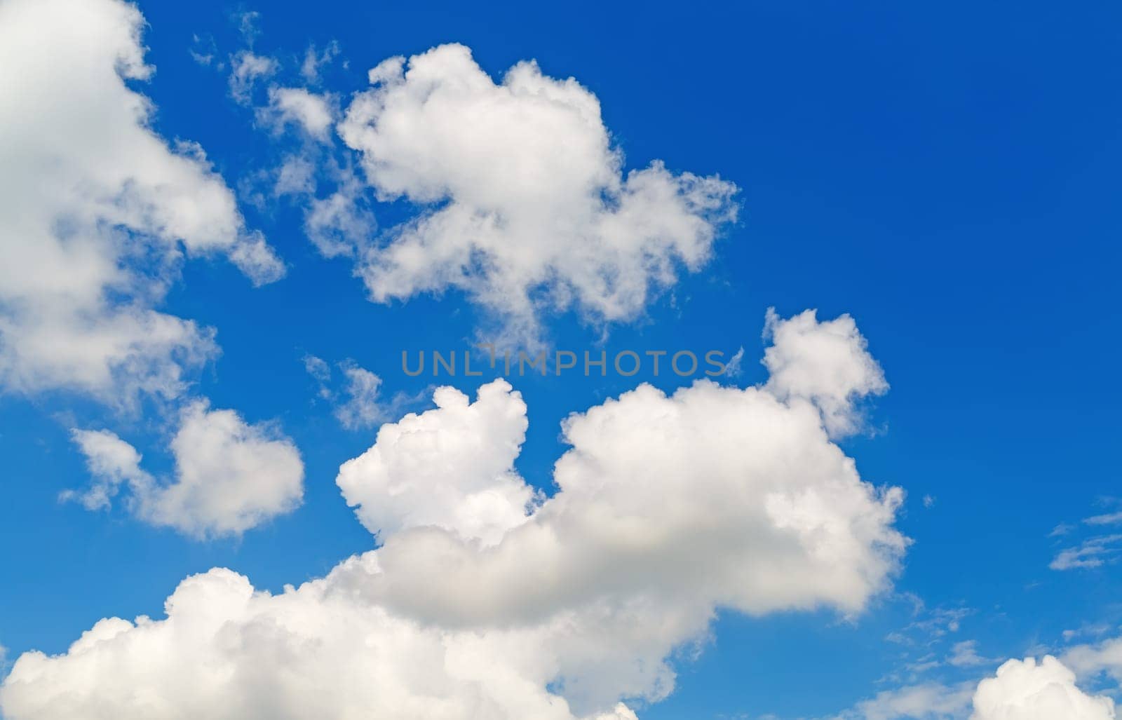Blue sky background with white cumulus clouds on a sunny day.