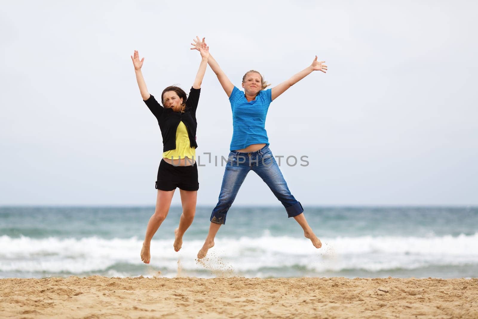 Two happy girls jumping on the beach against the sea and cloudless sky. Shallow depth of field. Focus on the model.