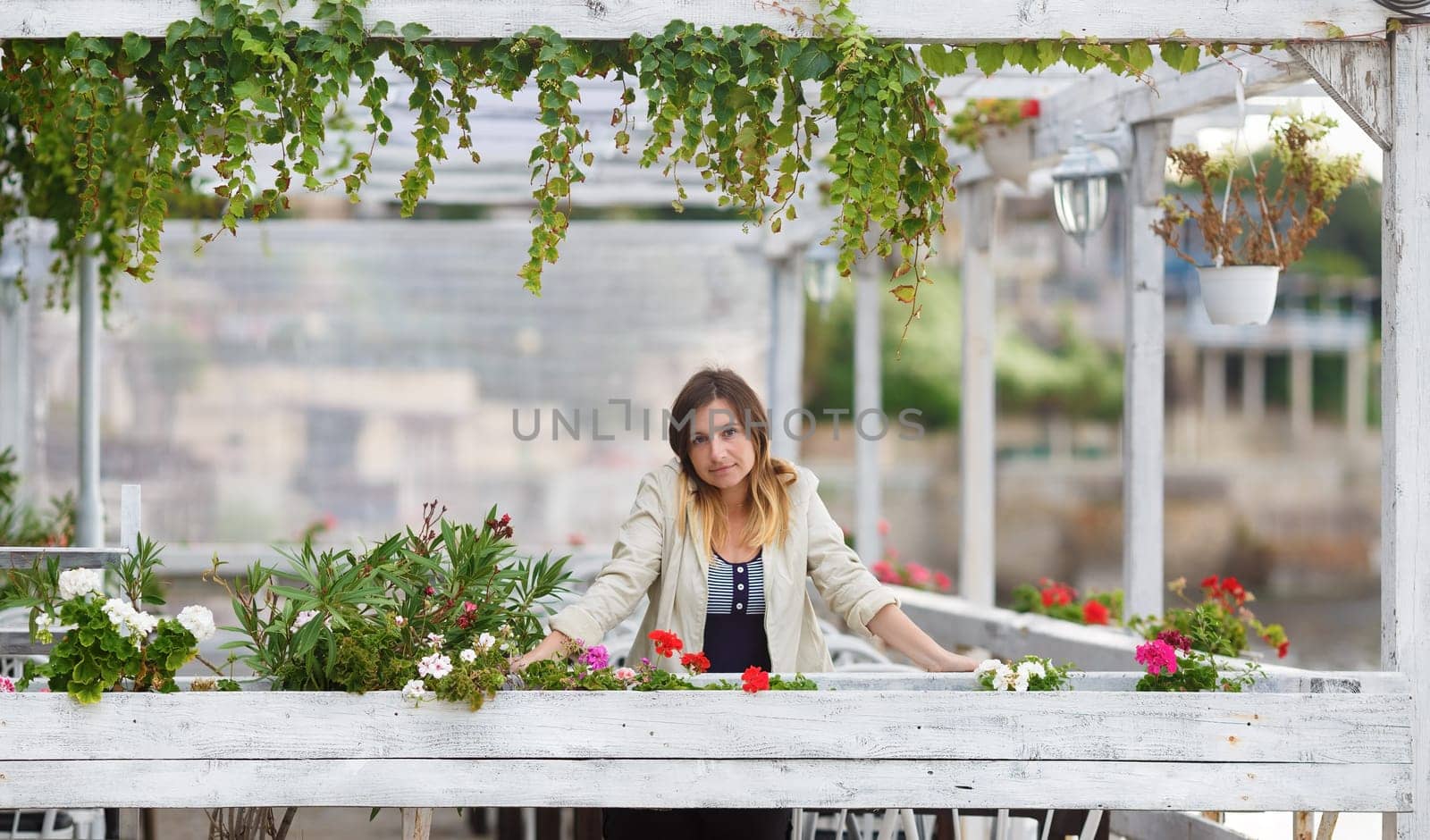Portrait of a pretty young woman in a vintage setting. Framing of the pure white paint wooden structures with ivy and flowers. Shallow depth of field. Focus on foreground and model.
