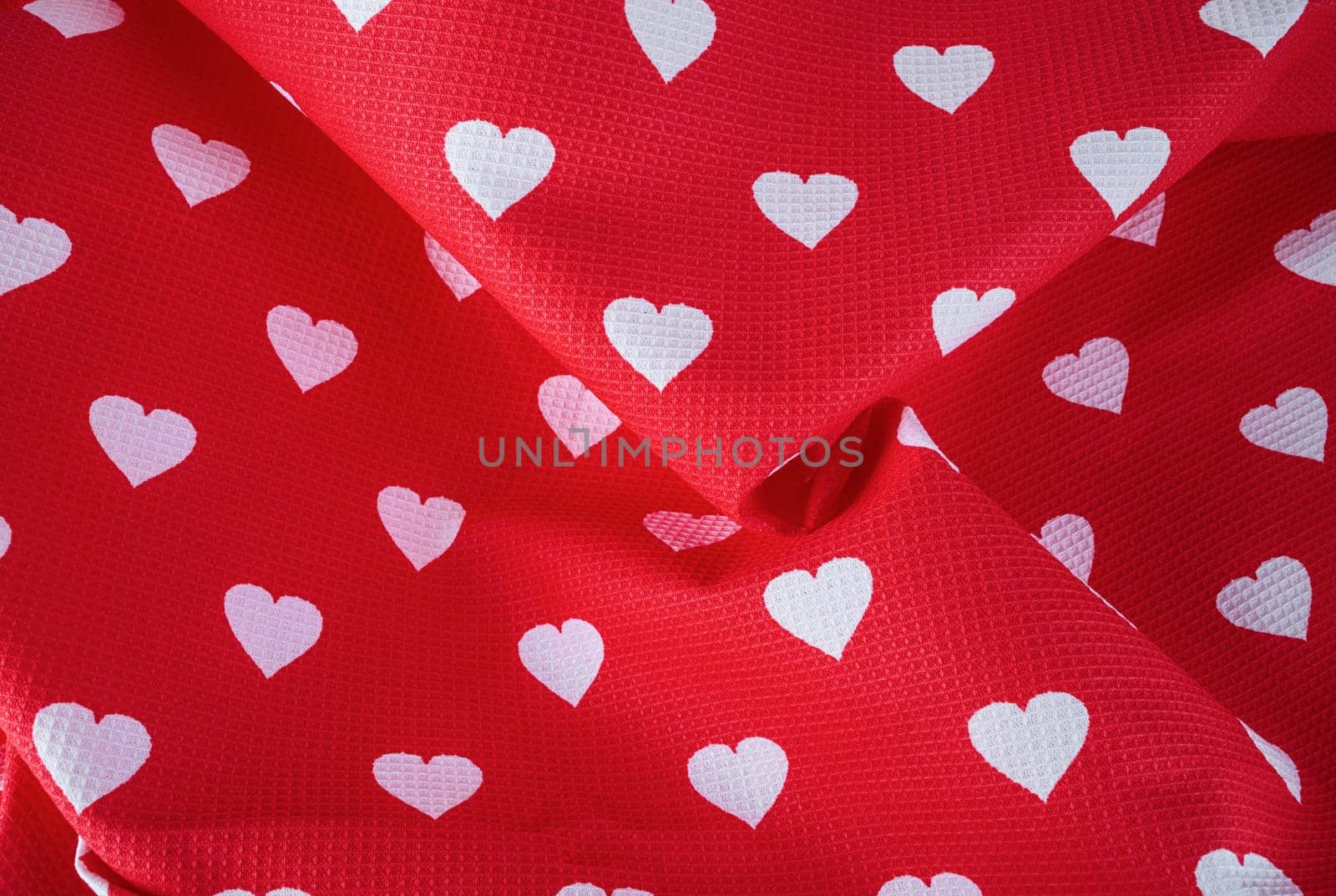 Pattern of white hearts on a bright red fabric with pleats. Top view.