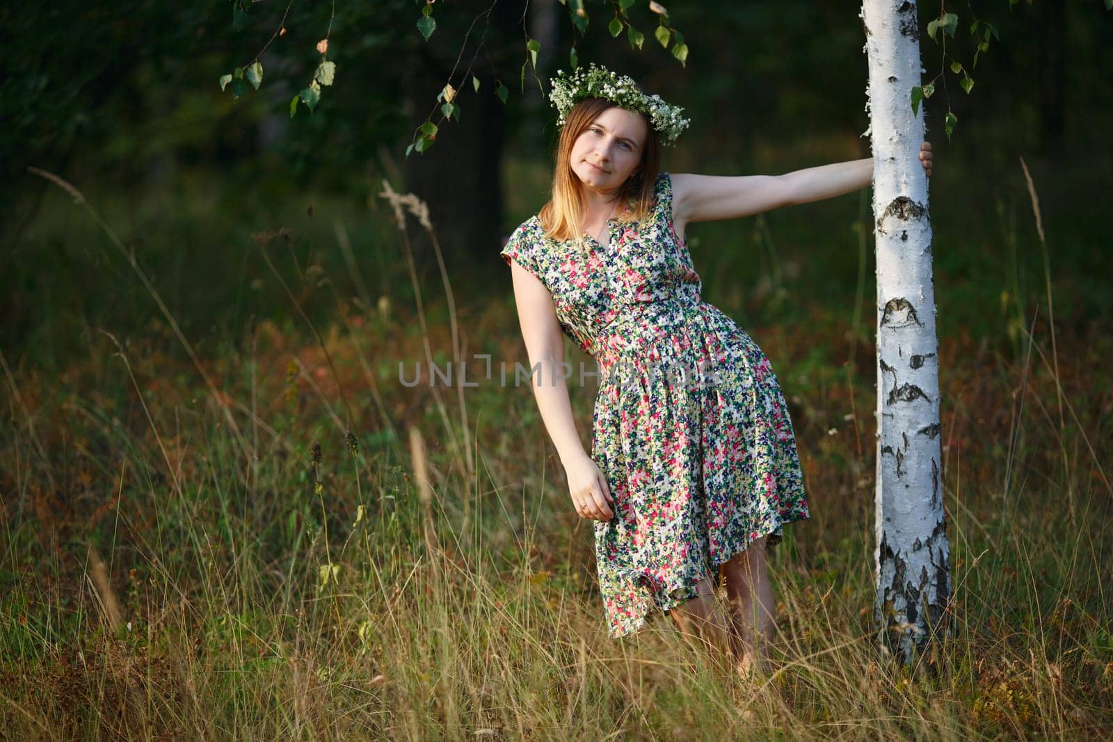 Girl with a wreath on his head keeps for birch. Sunset light. Shallow depth of field. Focus on model.