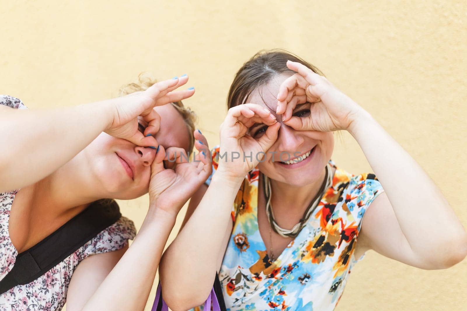 Pretty young women posing for photos put his hands to his eyes like binoculars. Two funny girls fooling around and grimaces. Shallow depth of field. Selective focus.