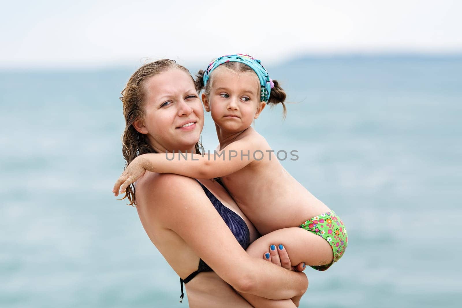 Mother and daughter at the hands of a blurred background of the sea. Focus on the models.