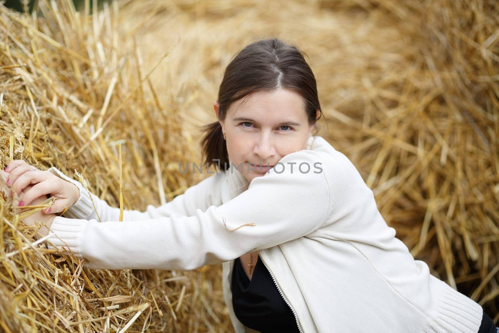 Pretty young woman in a white blouse posing on a straw background.