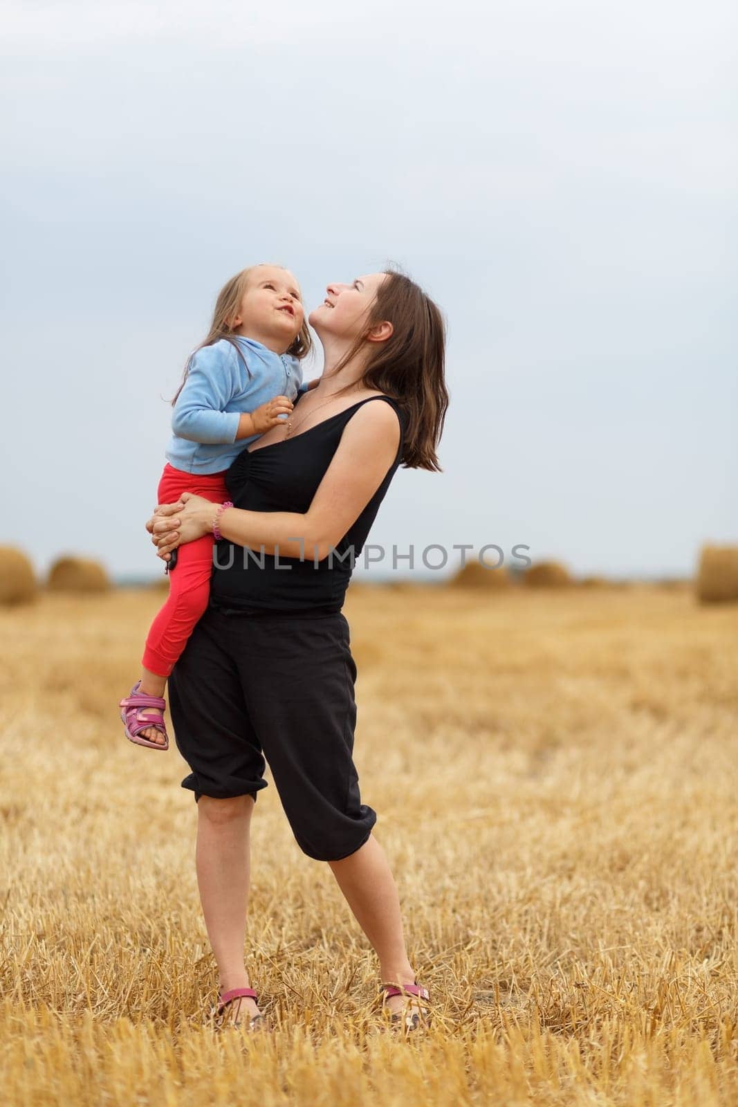 Mother and baby daughter in his arms in the straw field. Shallow depth of field. Selective focus.