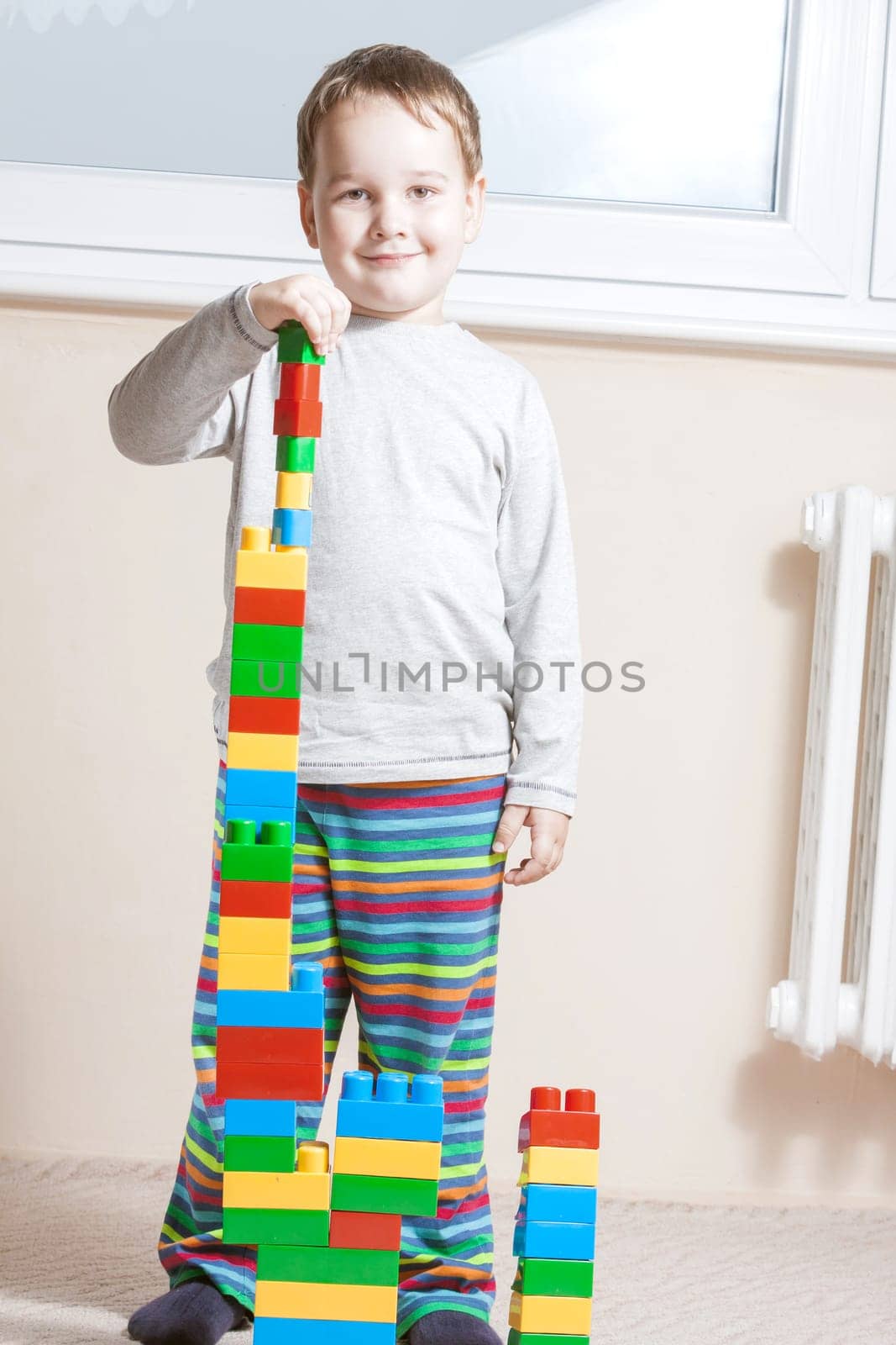 standing and smiling boy with built stack of colored cubes