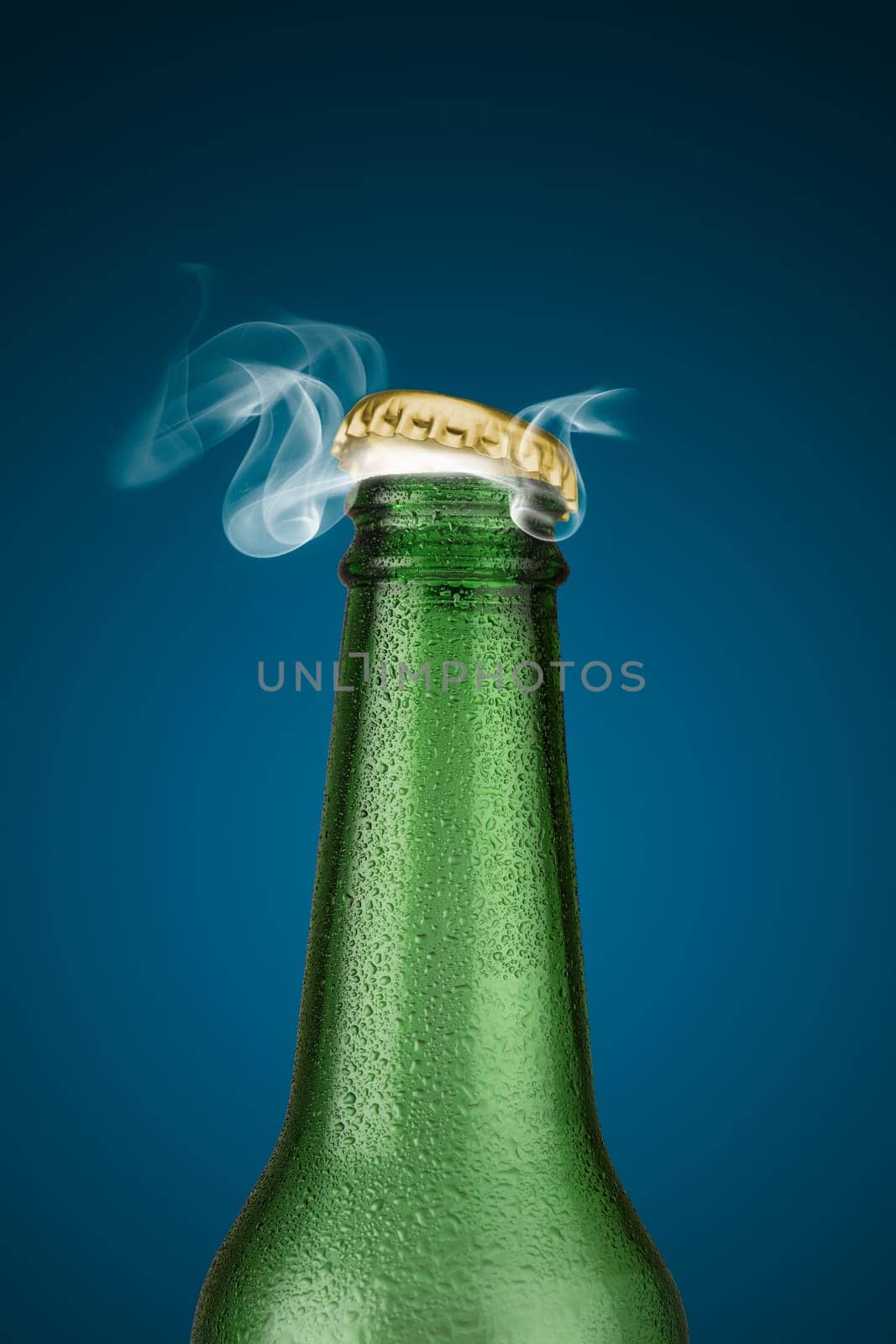 Green cold beer bottle with water drops and golden cap open on blue background
