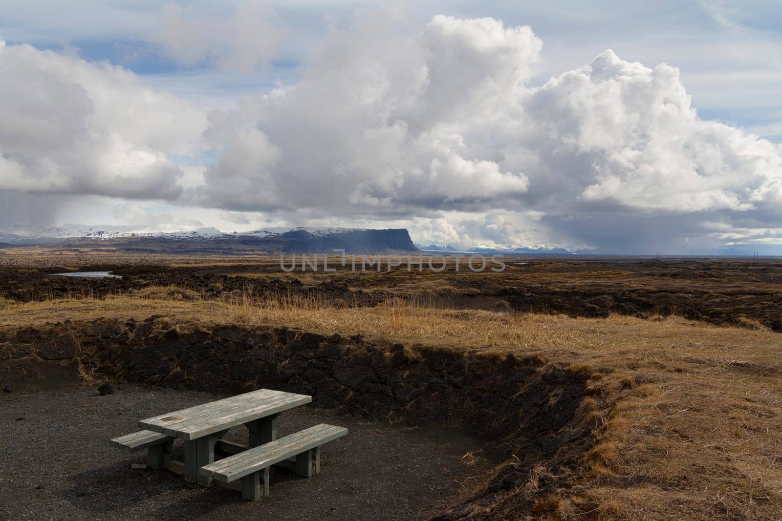 Horizontal panorama of a wooden resting bench with mountains covered in snow and dramatic clouds above