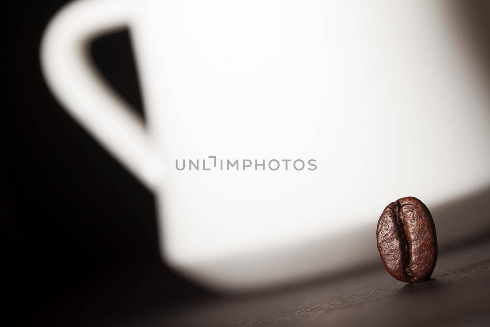 Macro shot of a coffee bean with a white coffee cup silhouette in the background