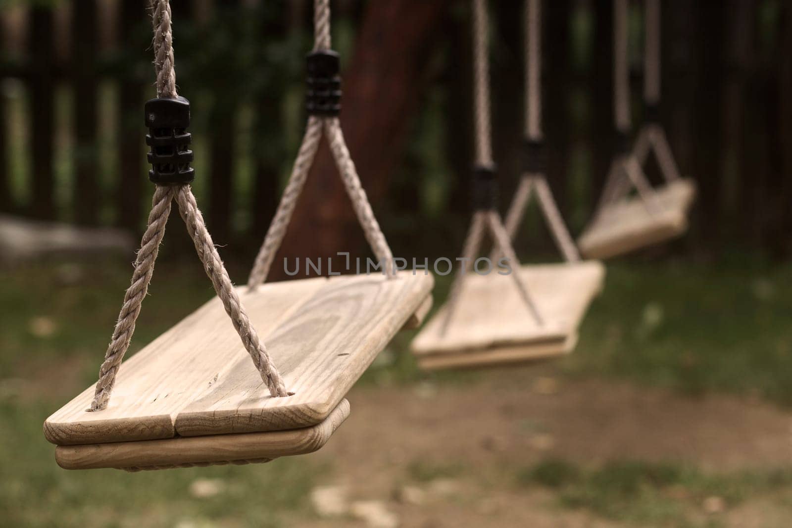 Horizontal perspective view of three wooden child swings in the park with shallow depth of field