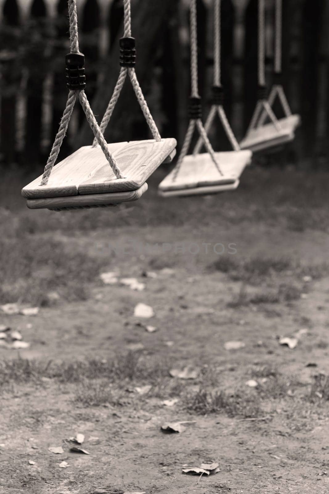 Vertical perspective view of three wooden child swings in the park with shallow depth of field