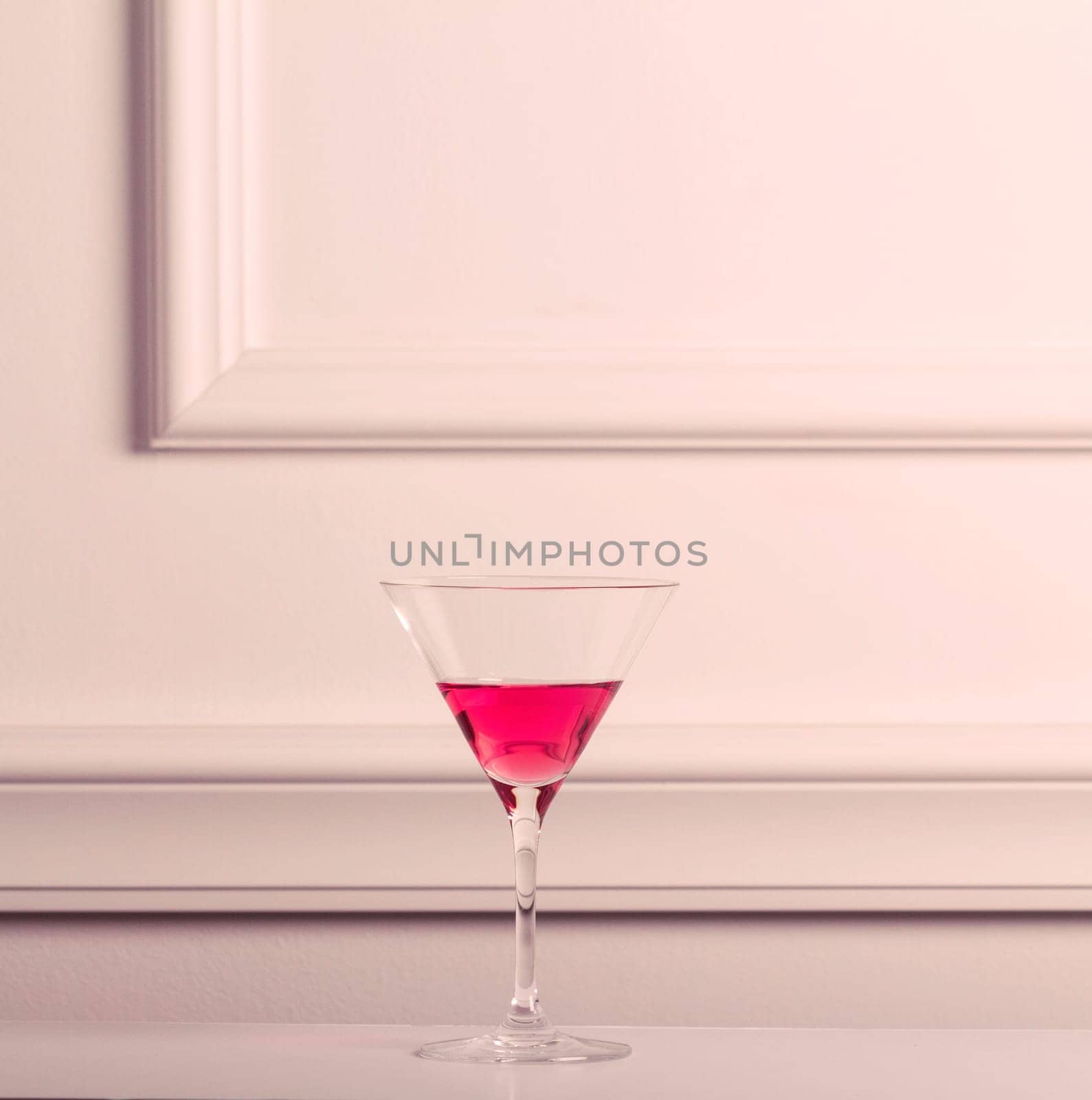 Lonely cocktail glass with pink liquid against an elegant wall.