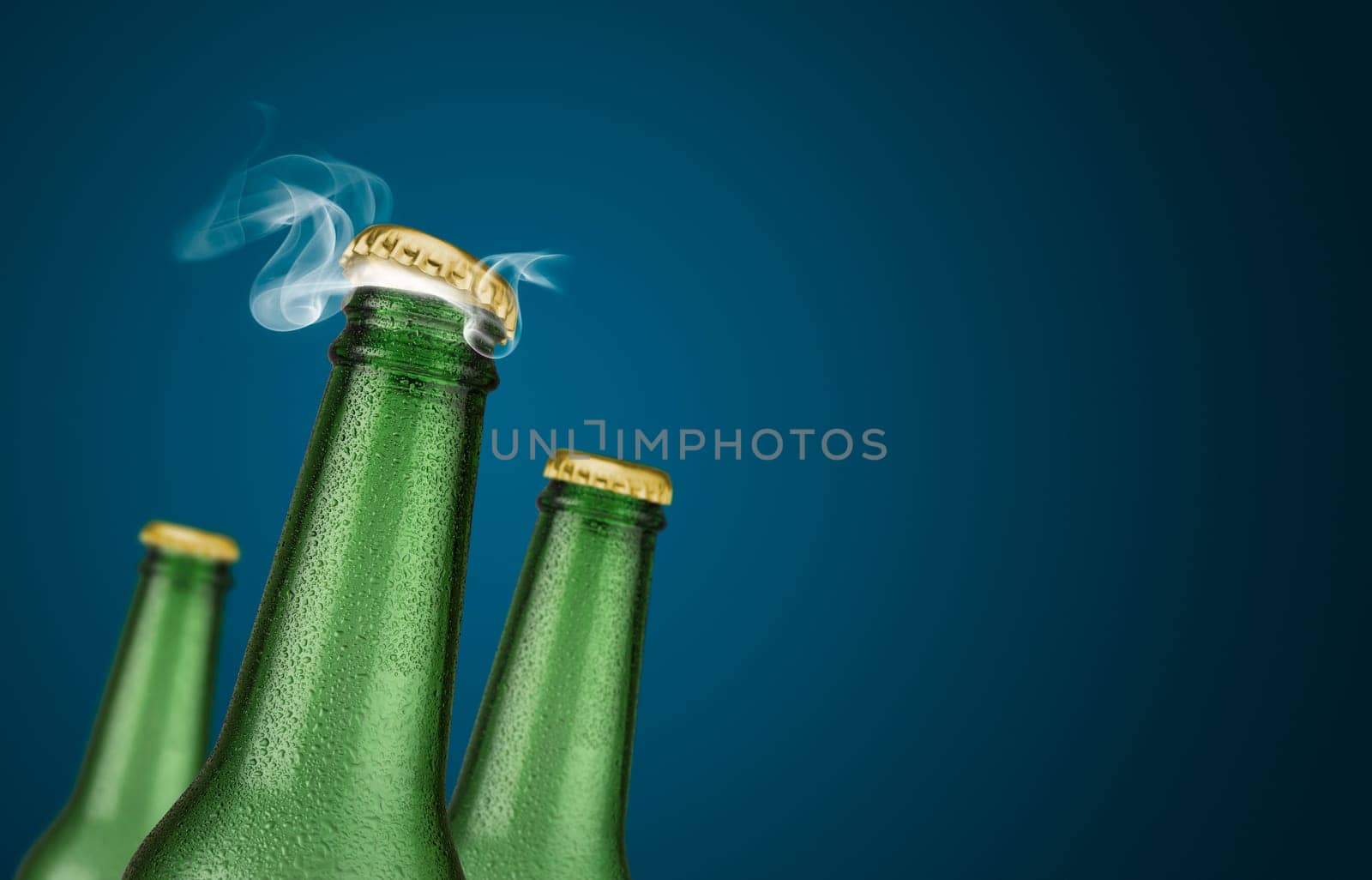 Horizontal photo of three green cold beer bottles with water drops and golden cap open on blue background