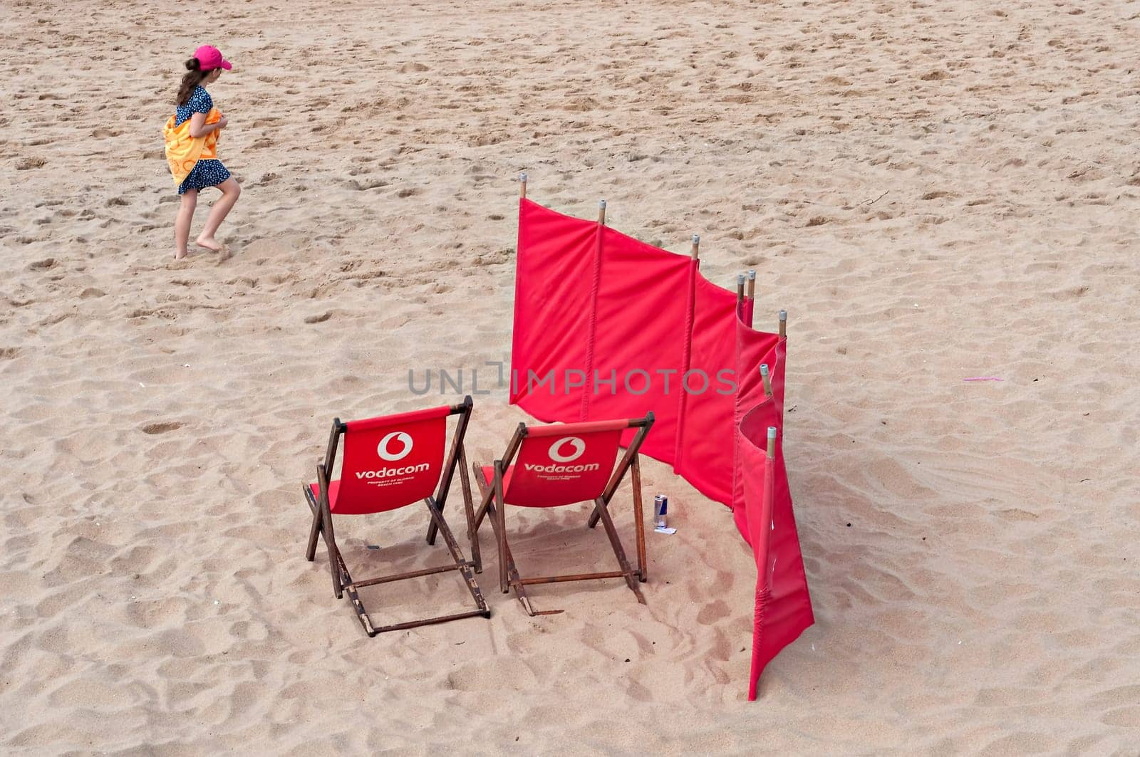 DURBAN, SOUTH AFRICA - JULY 09, 2016: Young girl walks past two Vodacom beach chairs on the beach in Umhlanga Rocks