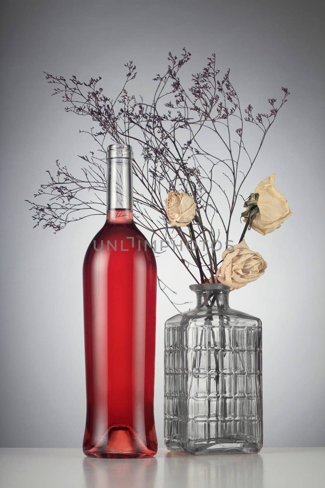 Rose wine bottle with no label next to withered white roses in a vase