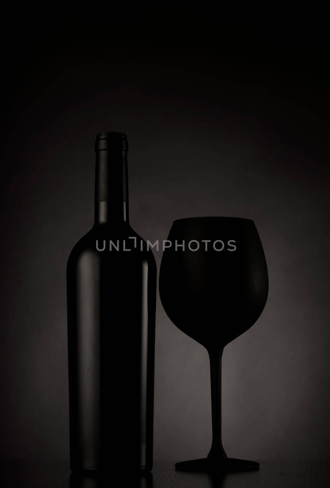 Black wine bottle and black glass of wine on black background