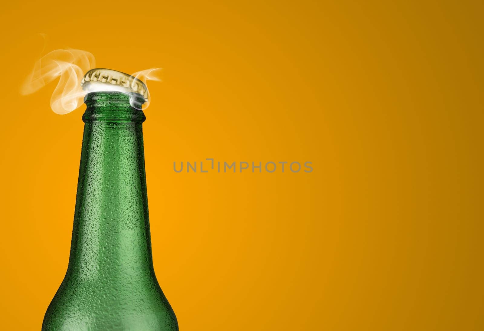 Horizontal photo of a green cold beer bottle with water drops and golden cap open on yellow background