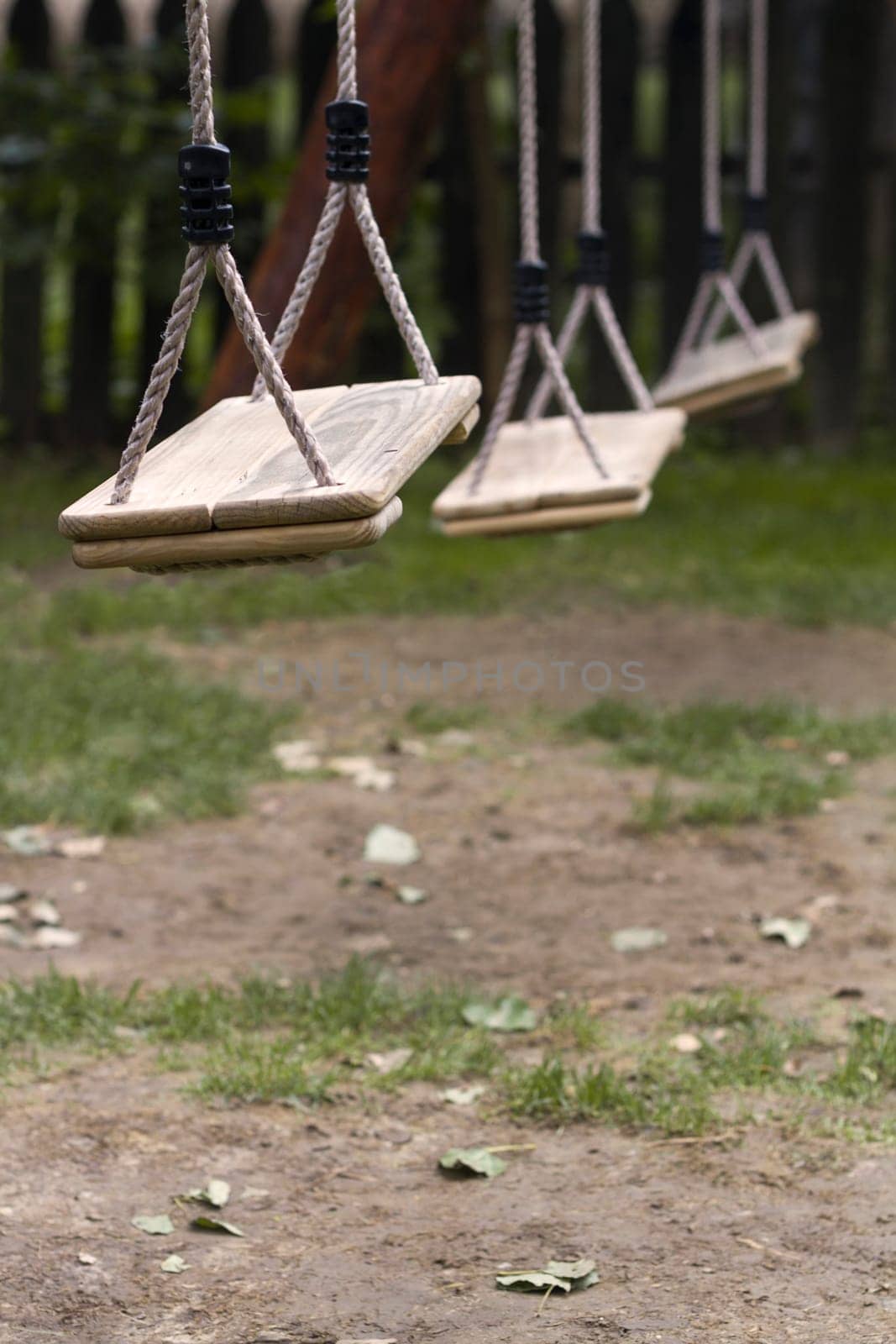 Vertical perspective view of three wooden child swings in the park with shallow depth of field