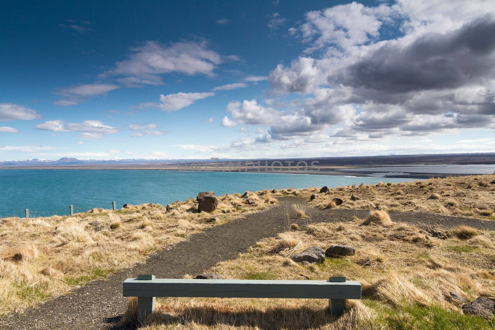 Horizontal panorama of a wooden resting bench with a beautiful shoreline in the background and dramatic clouds above