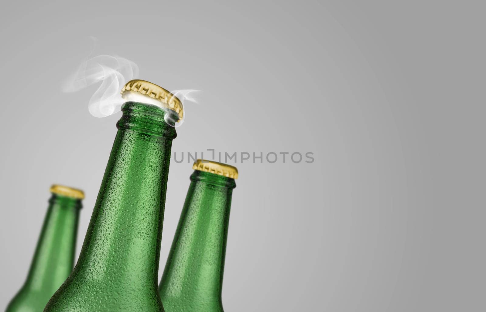 Horizontal photo of three green cold beer bottles with water drops and golden cap open on grey background