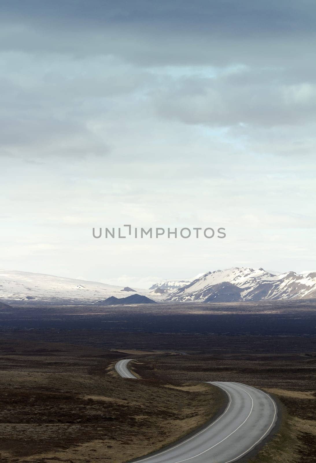 Vertical photo of a winding asphalt road going into the mountains in Thingvellir national park in Iceland