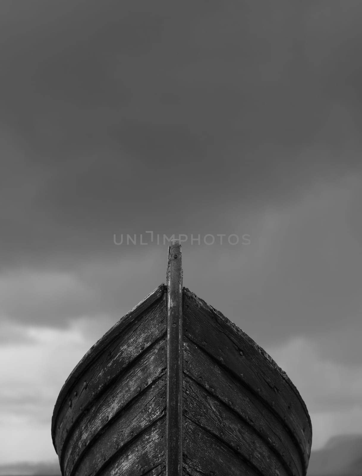 Vertical front view of an old fishing wood boat with rusted nails with dramatic grey storm clouds in the background