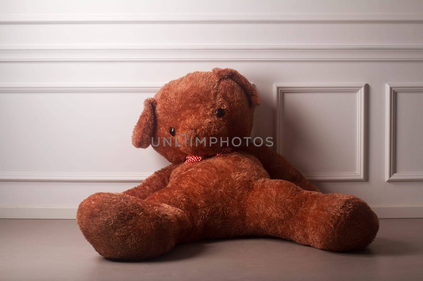 Huge toy bear with a dotted bow standing on the floor against the white wall of an empty room