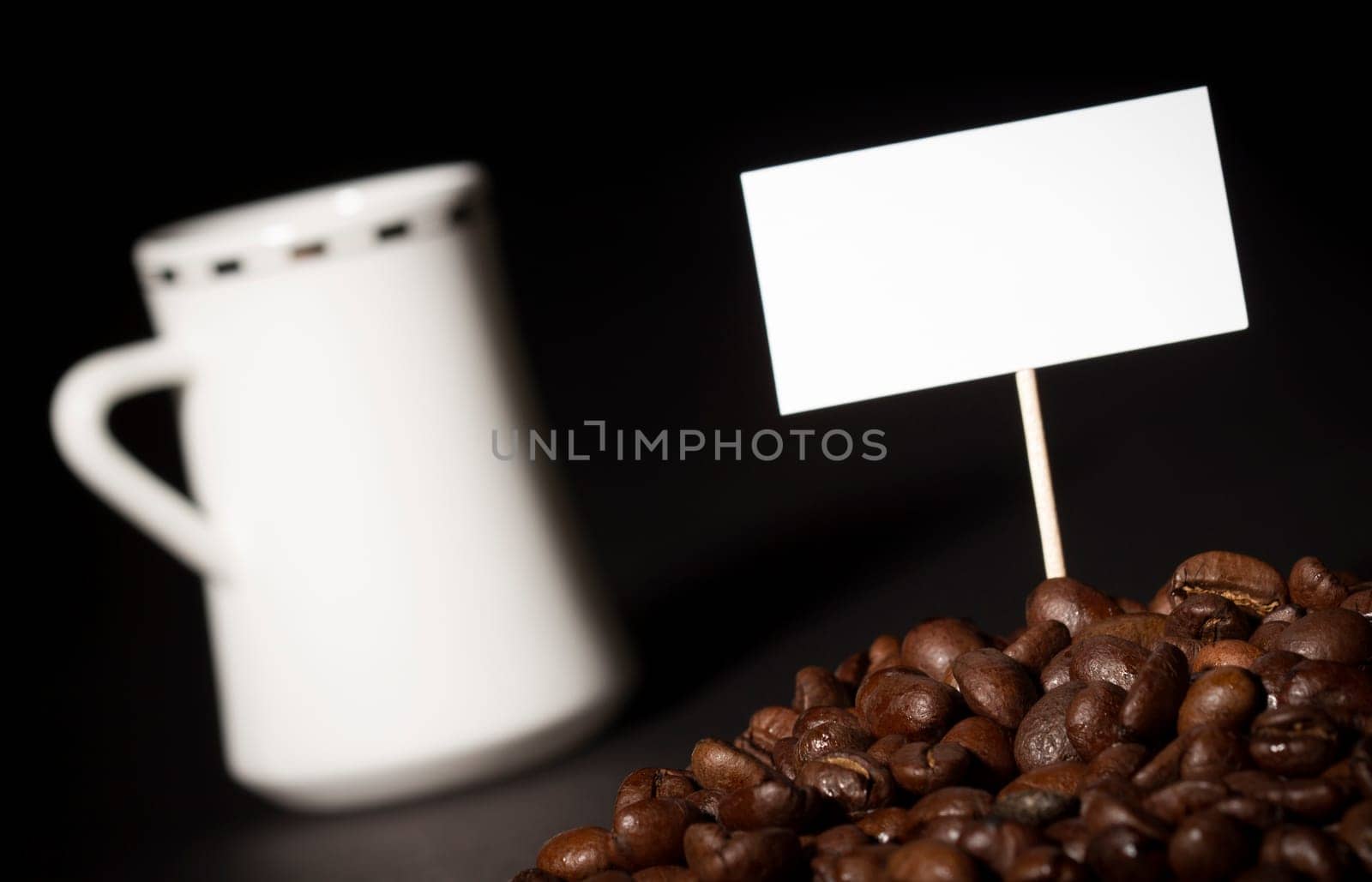 A pile of coffee beans with an empty sign on top of them and a white coffee cup in the background