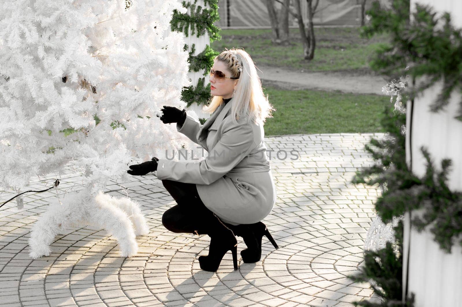 the beautiful woman in a gray coat sat down near a white fir-tree, a subject of the woman and holidays Christmas and New Year