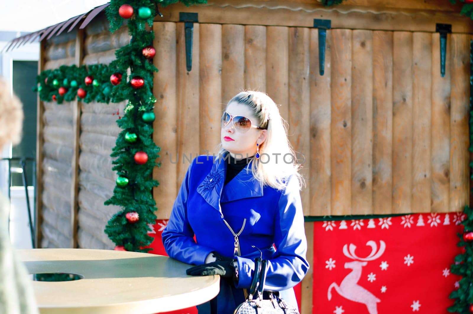 the beautiful woman at a table against the decorated wooden house for Christmas, a subject the woman and holidays Christmas and New Year