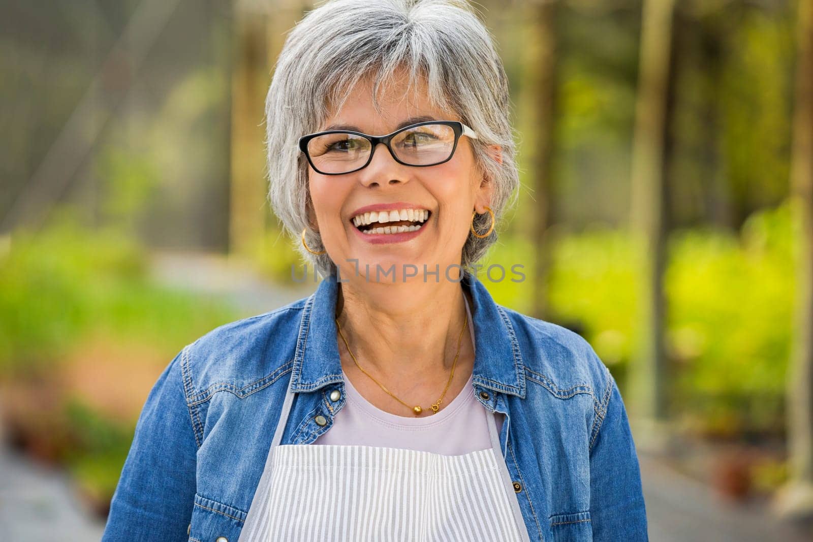 Beautiful mature woman working in a greenhouse, looking at camera while laughing