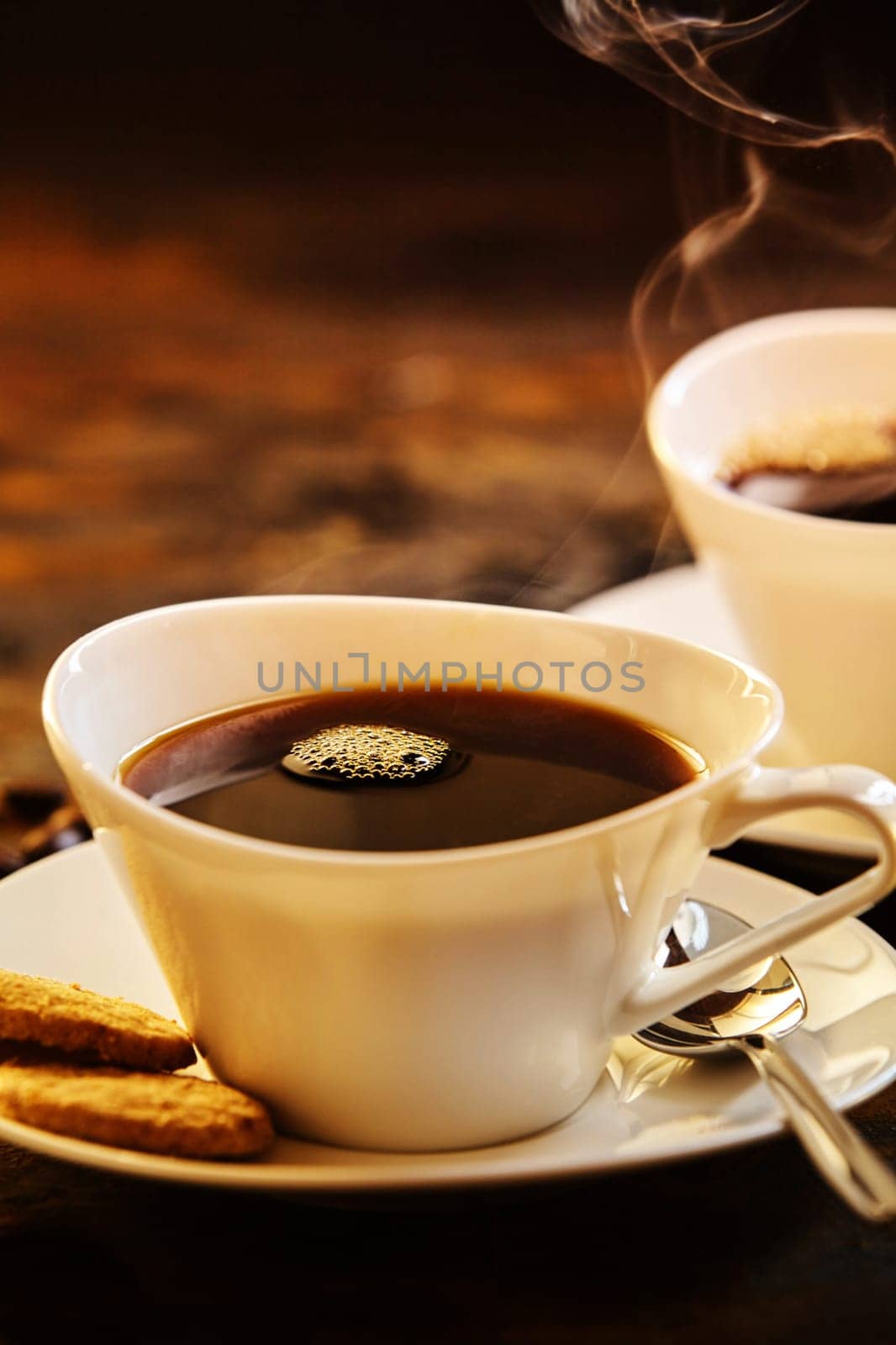 Close up on two servings of delicious hot coffee with spoon and biscuits in porcelain saucer