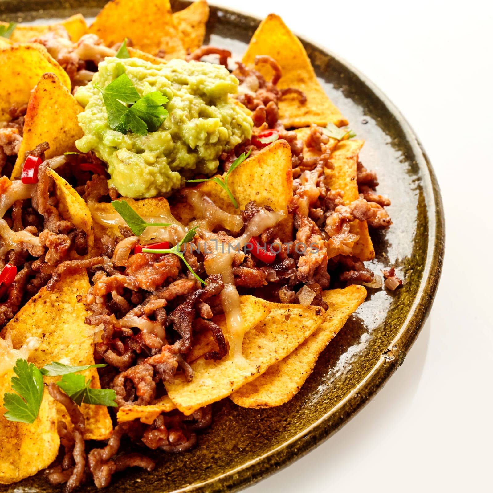 Close up cropped view on round ceramic plate of yellow corn tortilla chips, cheese and beef garnished with cilantro and red peppers