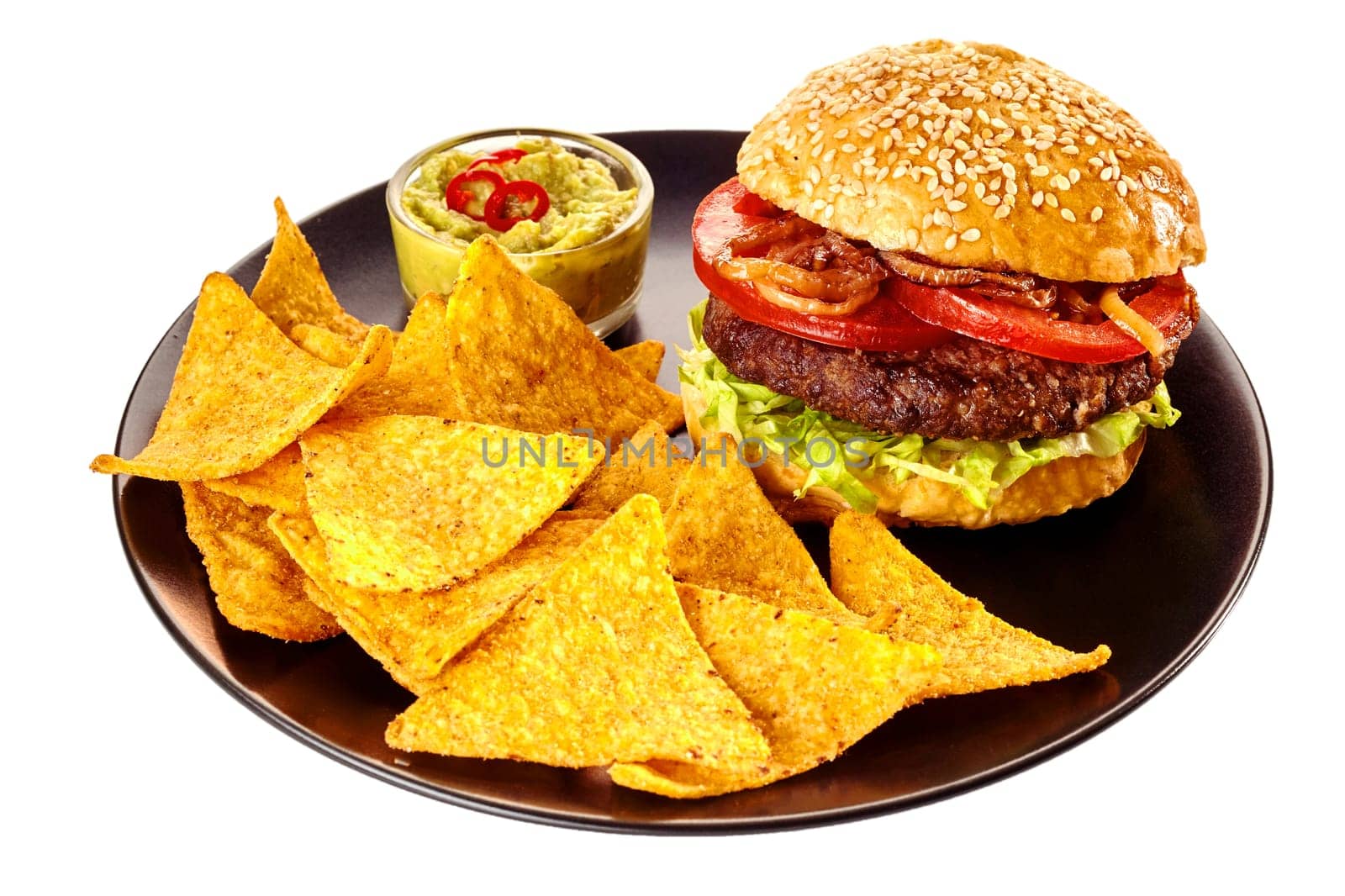 Isolated round black plate of nacho tortilla chips, guacamole and hamburger topped with tomatoes and friend onions in sesame seed bun over white background