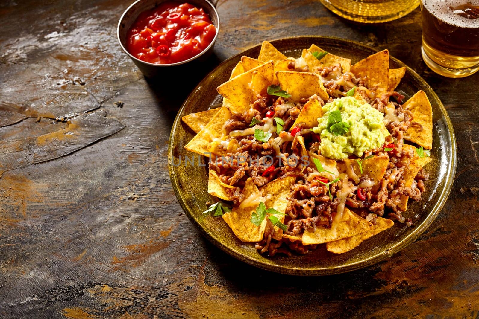 Delicious plate of yellow corn tortilla chips with cheese, meat, guacamole and red hot spicy salsa over table with copy space