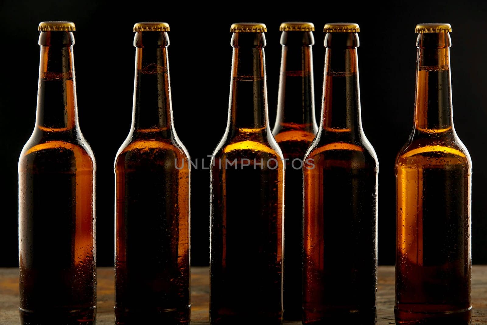 Row of ice cold unlabelled unopened brown beer bottles standing on a pub or tavern counter on a shadowy background in a branding and advertising concept for Oktoberfest