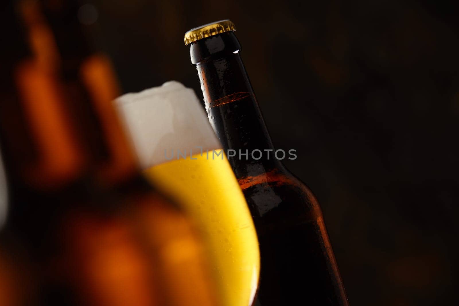 Glass of glowing golden frothy beer in a selective focus view between to beer bottles with copy space for Oktoberfest, tilted angle perspective